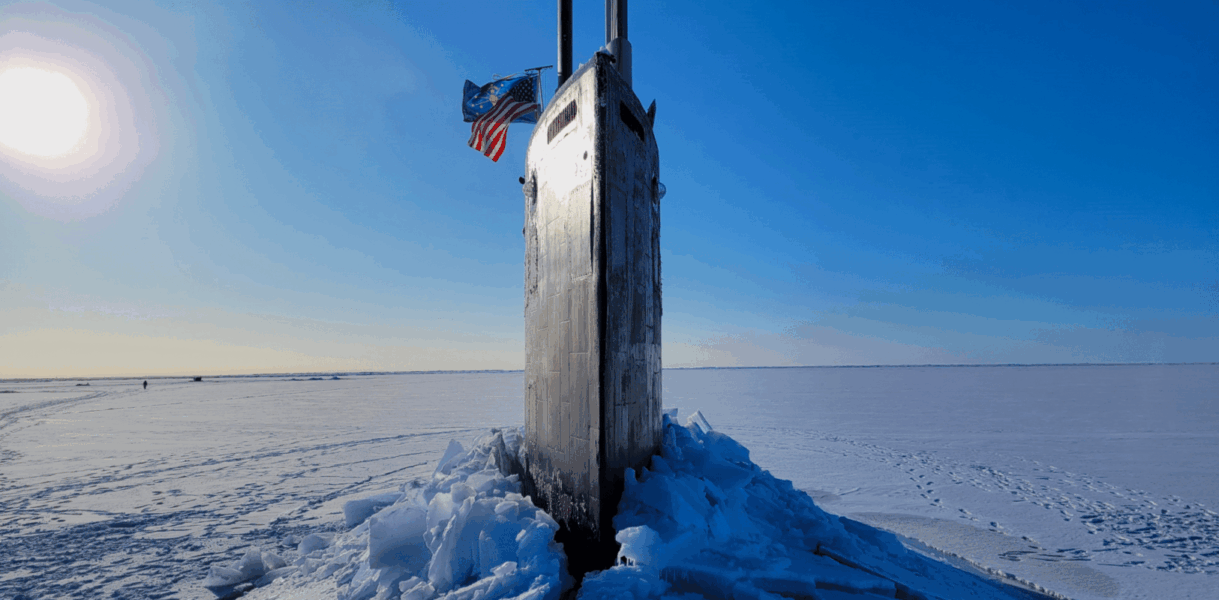 The USS INDIANA (SSN 789) at Ice Camp Whale, Beaufort Sea. The sail is seen breaking through the ice, with an American flag flying on the left.